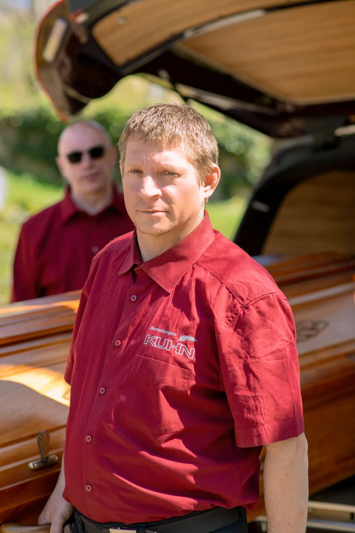 Kuhn Bestattungen Mitarbeiter beim Sargtransport, Fokus auf Einzelperson im Vordergrund