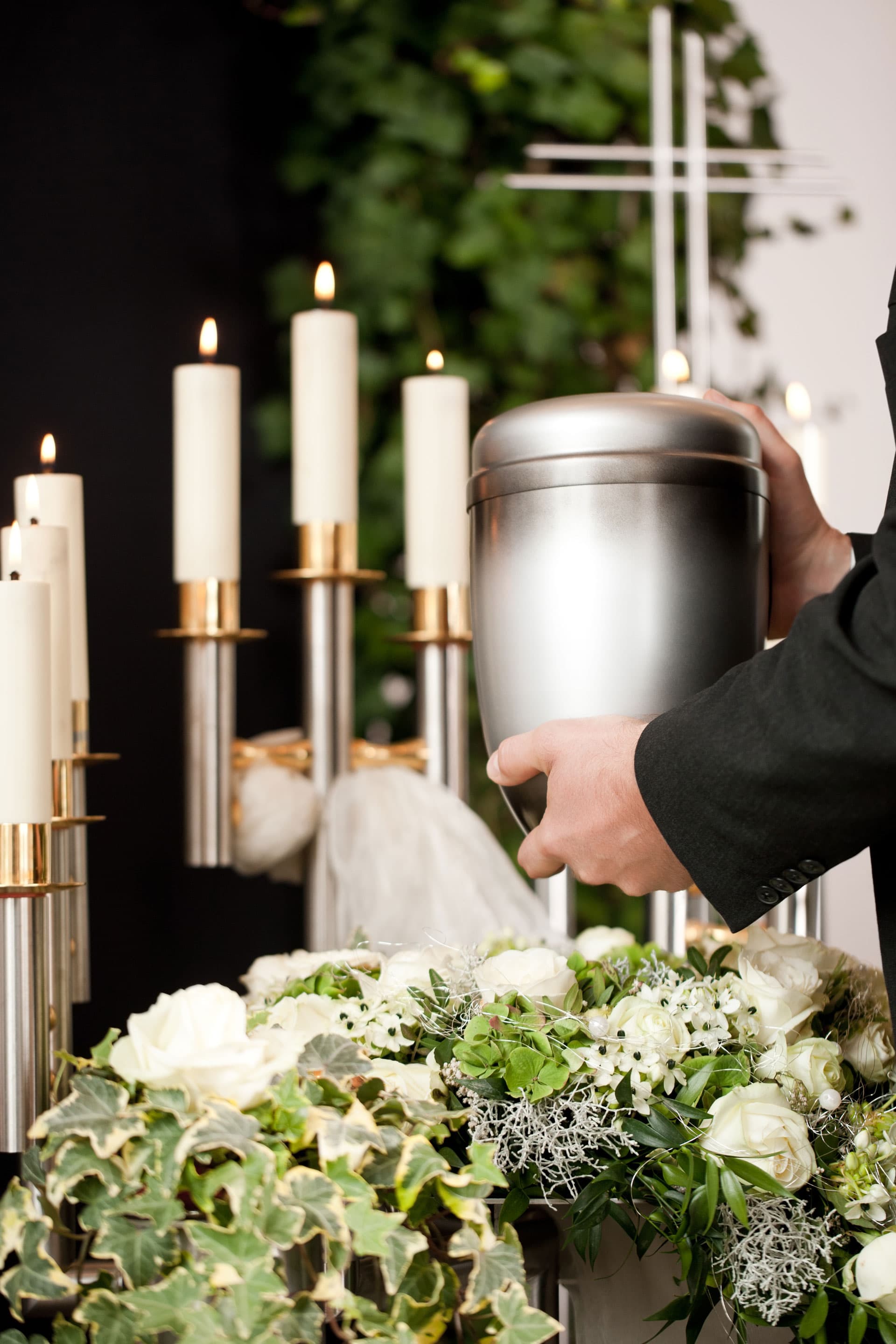Person hält silberne Urne während einer Trauerfeier mit Kerzen und Blumen bei Kuhn Bestattungen Asperg.