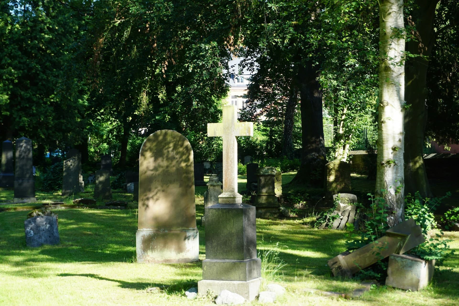 Historisches Steinkreuz auf einem schattigen Friedhof Historisches Steinkreuz auf einem schattigen Friedhof mit alten Grabsteinen und dichtem Baumbestand.
