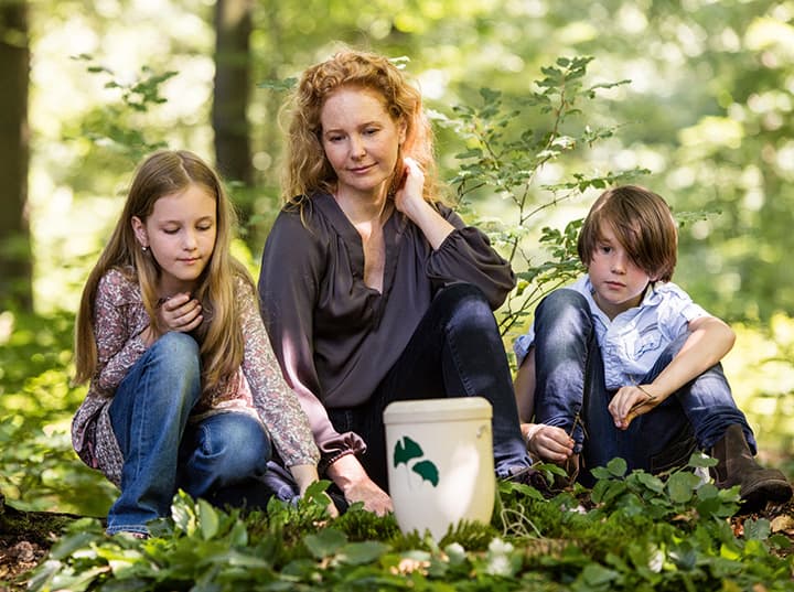 Familie bei einer FriedWald-Bestattung mit Urne im Wald.